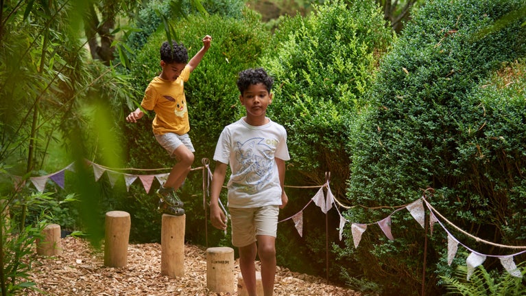 Two young boys walking between hedges through the garden in summer at Nymans, West Sussex
